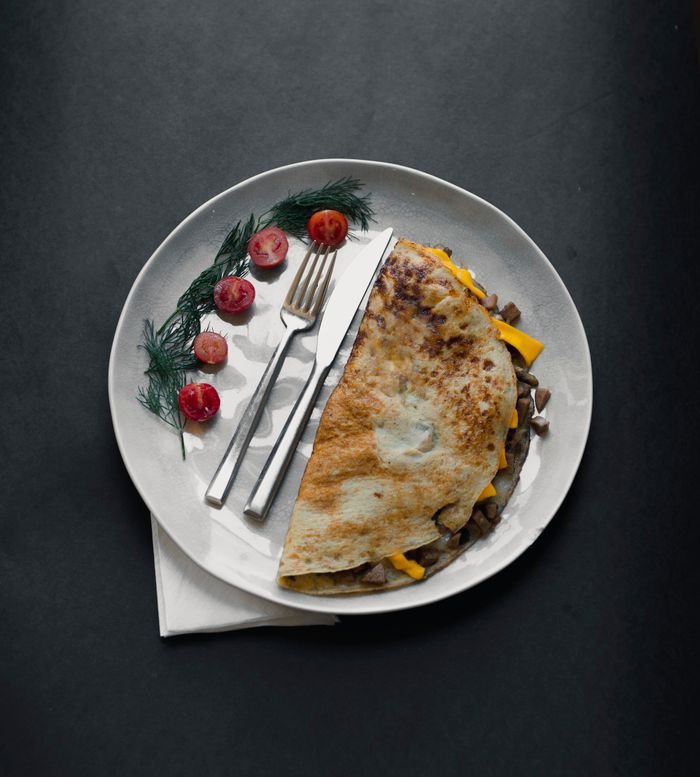 Mastering the First Impression: Your intriguing post title goes here Tasty omelette paired with cherry tomatoes and fresh herbs, served elegantly on a white plate.