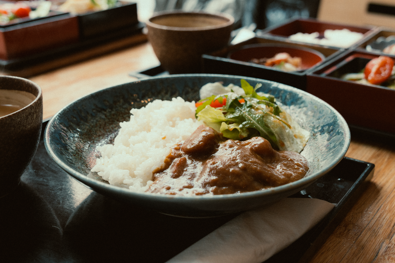 Home A close-up of a Japanese curry rice dish with salad served in a ceramic bowl.